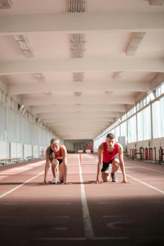 una chica y un chico preparados en la línea de salida de una pista de atletismo