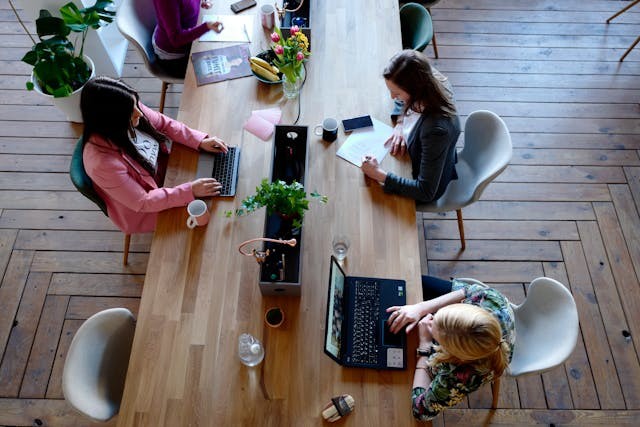 vista aérea de mesa de madera con tres chicas sentadas con sus portátiles