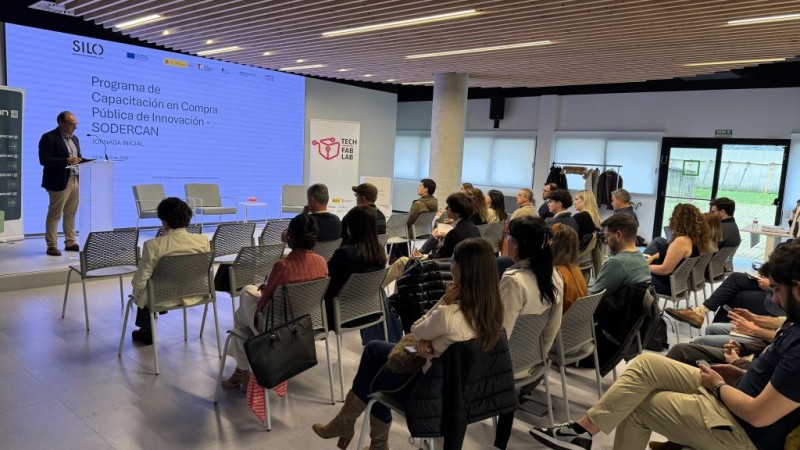 persona en escenario con público en sillas de espaldas a la cámara