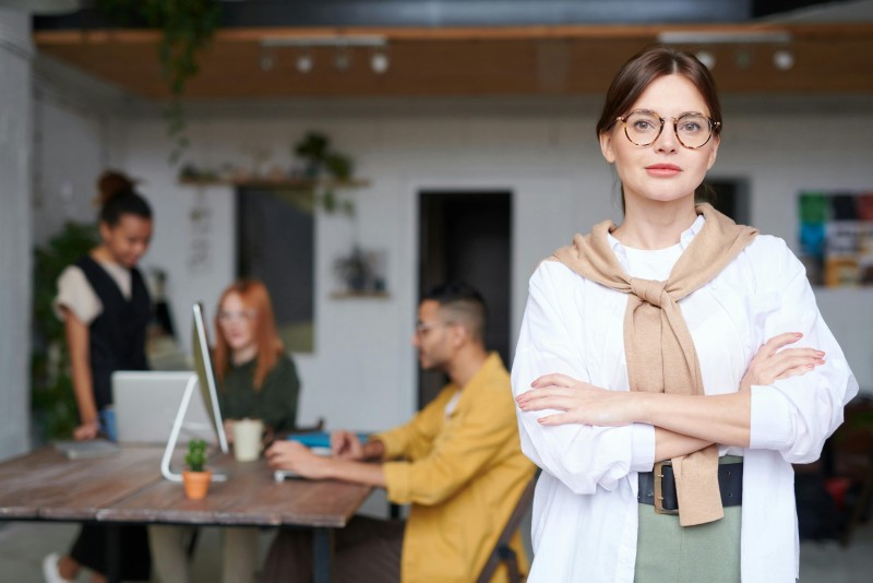 chica con gafas y brazos cruzados en primer plano con grupo trabajando de fondo